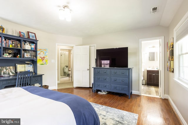 bedroom featuring lofted ceiling, visible vents, dark wood finished floors, baseboards, and ensuite bath