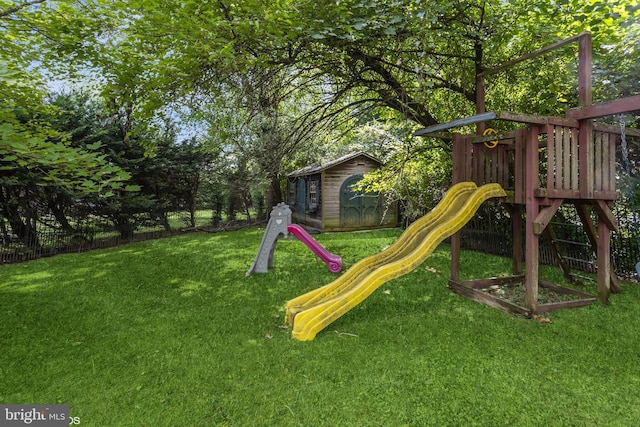 view of jungle gym featuring a storage shed, fence, a lawn, and an outbuilding