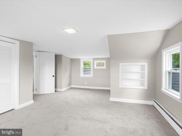 additional living space featuring baseboard heating, built in shelves, light colored carpet, and a wealth of natural light