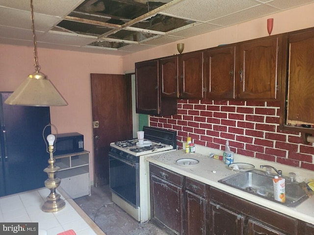 kitchen featuring white gas stove, dark brown cabinetry, pendant lighting, a paneled ceiling, and sink