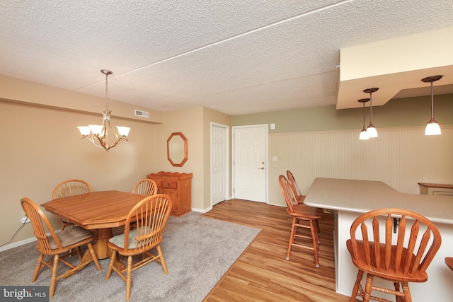 dining space with a textured ceiling, an inviting chandelier, and light wood-type flooring