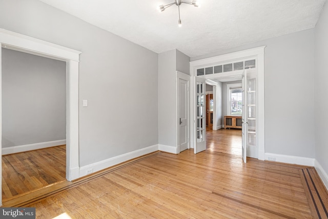 empty room with a textured ceiling, light hardwood / wood-style flooring, and french doors