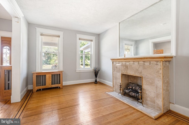 unfurnished living room featuring a tiled fireplace, a textured ceiling, and light hardwood / wood-style flooring