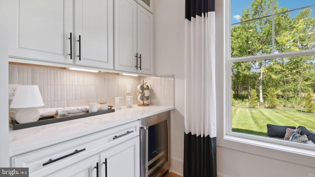 bar featuring white cabinets, backsplash, wine cooler, and light stone countertops