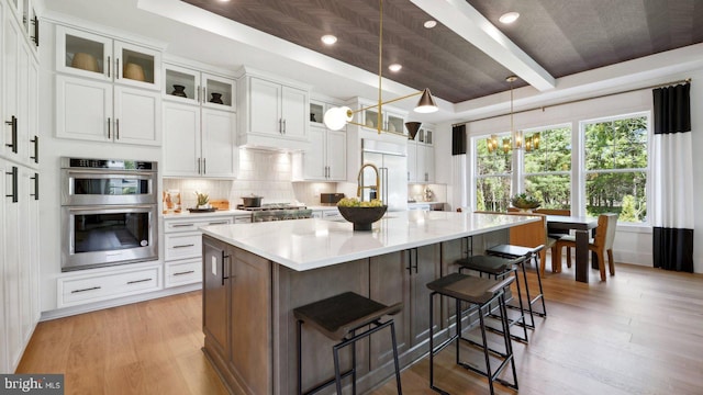 kitchen with decorative light fixtures, light hardwood / wood-style flooring, an island with sink, stainless steel appliances, and white cabinets