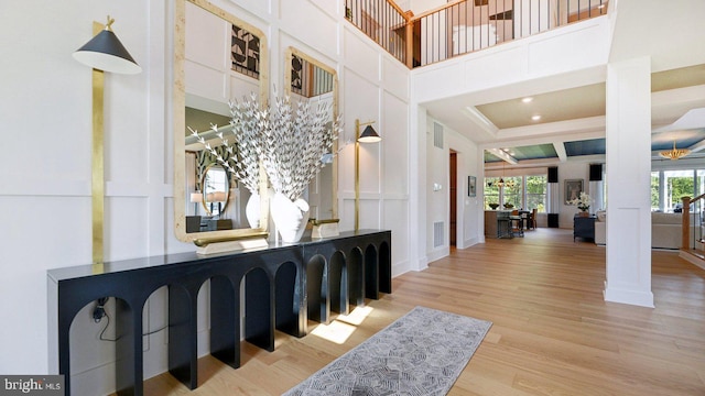 foyer entrance with a high ceiling, decorative columns, wood finished floors, and visible vents