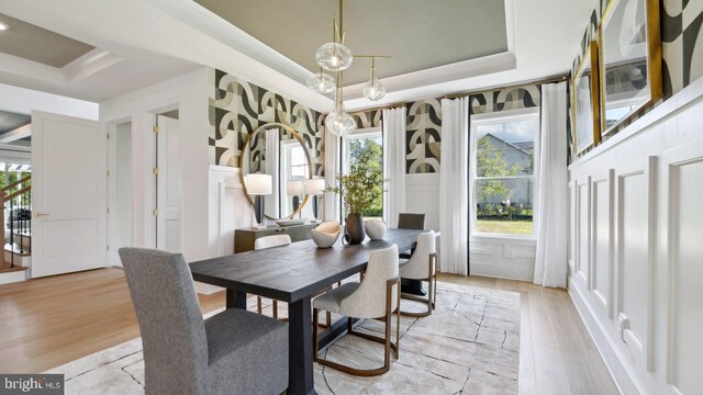 dining area with light wood-type flooring, a tray ceiling, and a healthy amount of sunlight