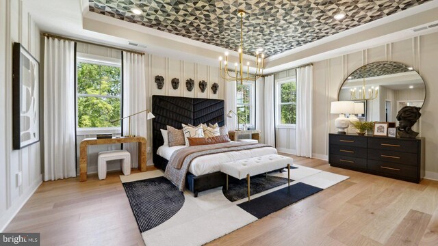 bedroom featuring a raised ceiling, light wood-type flooring, and multiple windows