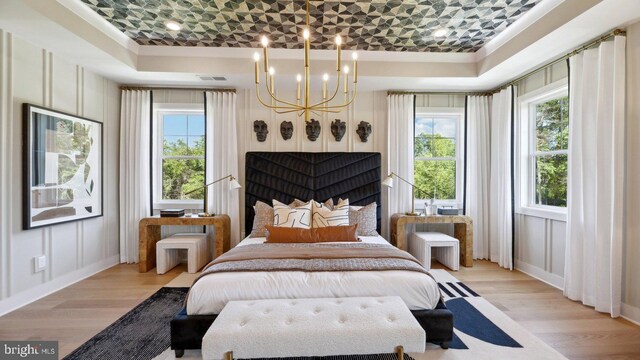 bedroom with light wood-type flooring, a raised ceiling, and a chandelier