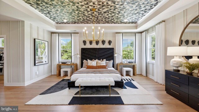 bedroom with a raised ceiling, light hardwood / wood-style flooring, and an inviting chandelier