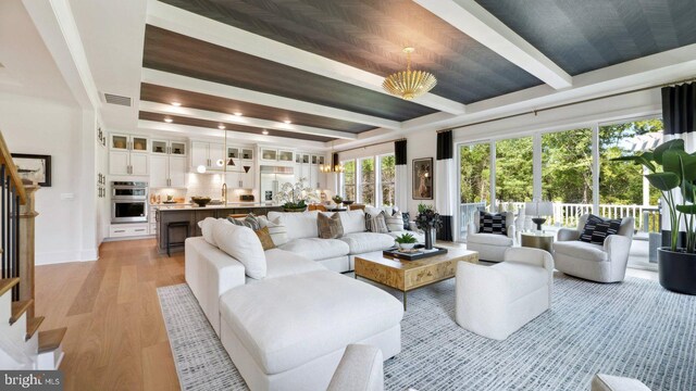 living room featuring plenty of natural light, a notable chandelier, beam ceiling, and light hardwood / wood-style floors