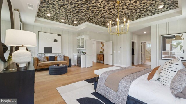 bedroom with a tray ceiling, light hardwood / wood-style flooring, wine cooler, and a notable chandelier