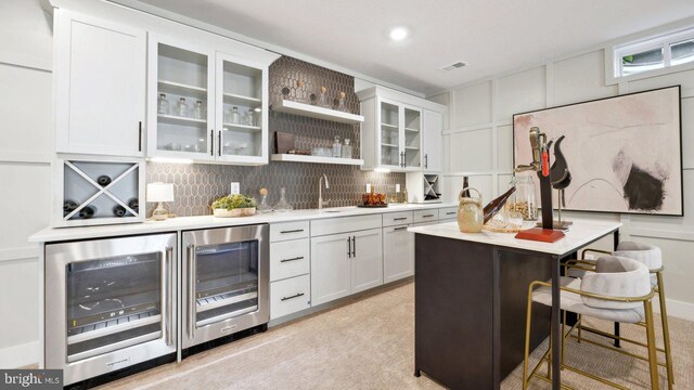 bar featuring white cabinets, wine cooler, and light carpet