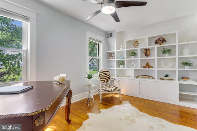 office area with baseboards, light wood finished floors, visible vents, and a ceiling fan