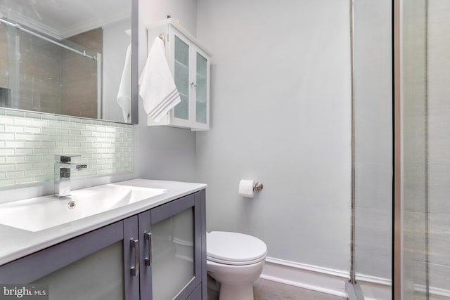 bathroom with toilet, vanity, baseboards, a tile shower, and tasteful backsplash