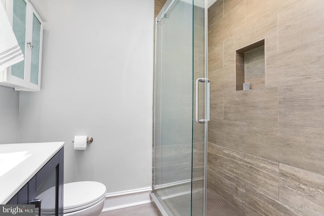 bathroom with toilet, a stall shower, vanity, and baseboards