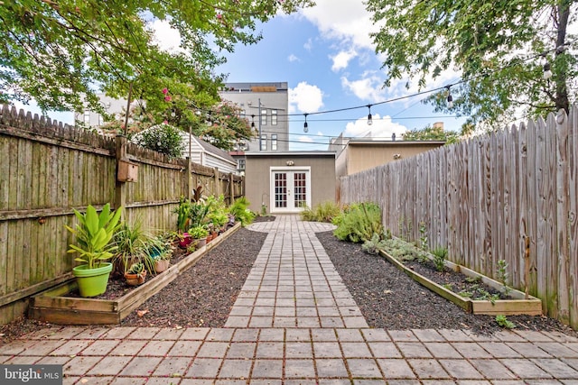 view of patio featuring a fenced backyard, a vegetable garden, an outdoor structure, and french doors