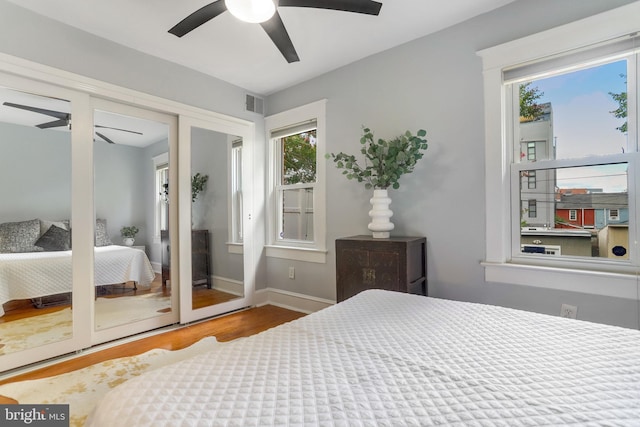 bedroom with a ceiling fan, visible vents, baseboards, and wood finished floors