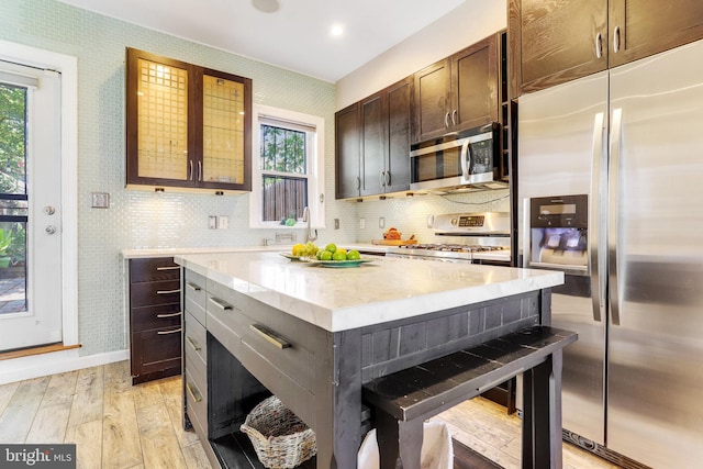 kitchen with appliances with stainless steel finishes, decorative backsplash, light wood-type flooring, a kitchen island, and a breakfast bar