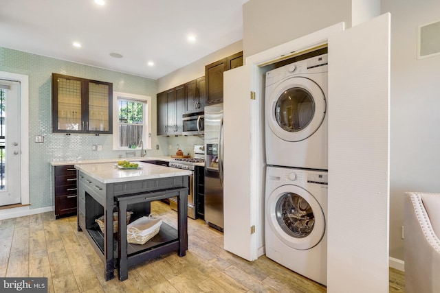 laundry room featuring baseboards, laundry area, light wood-type flooring, and stacked washer / drying machine