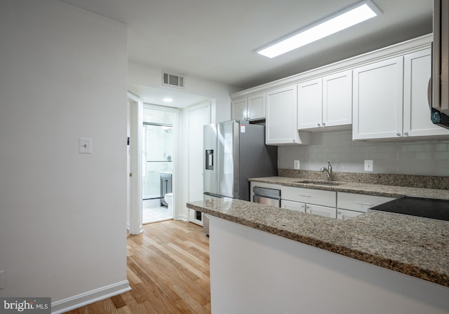 kitchen with stone counters, white cabinetry, backsplash, sink, and light hardwood / wood-style floors