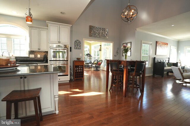 kitchen featuring dark countertops, dark wood-style flooring, decorative light fixtures, and stainless steel double oven