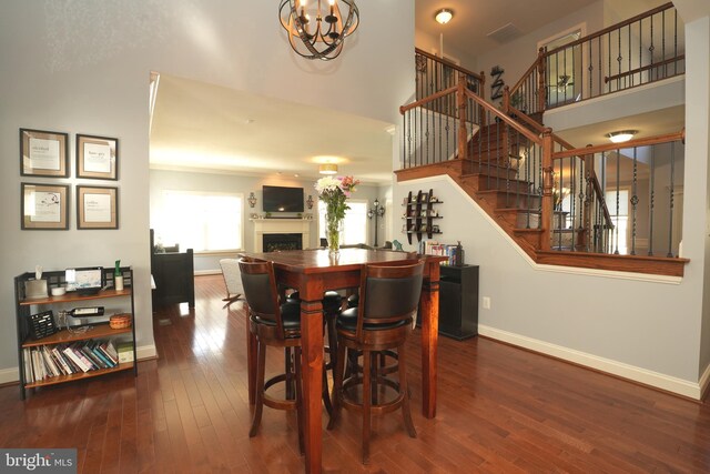 dining area featuring a fireplace, a towering ceiling, stairway, wood finished floors, and baseboards