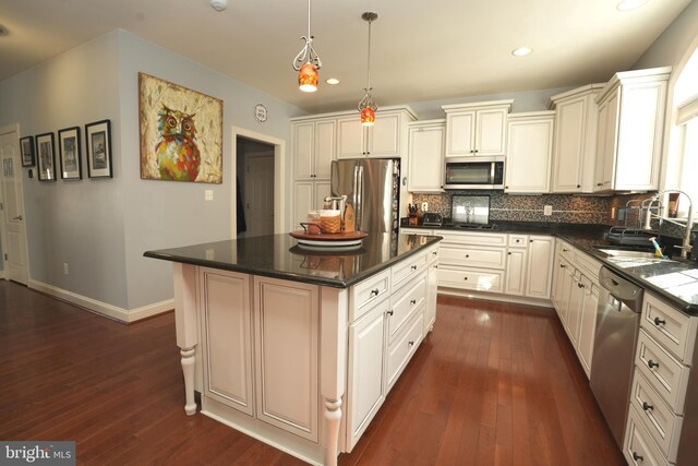 kitchen featuring decorative backsplash, appliances with stainless steel finishes, a center island, pendant lighting, and a sink