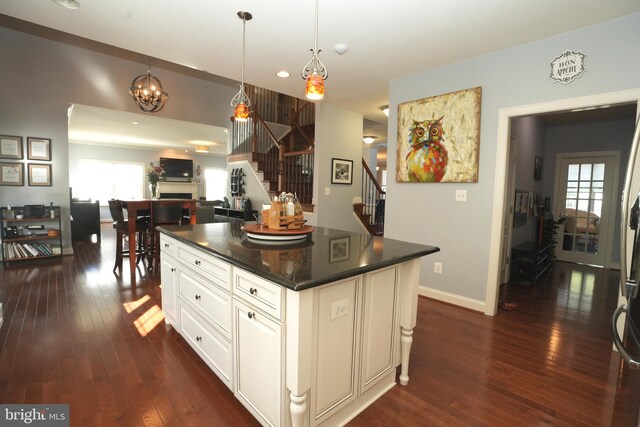 kitchen featuring white cabinets, open floor plan, a center island, decorative light fixtures, and a fireplace