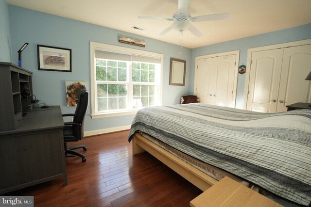 bedroom with baseboards, visible vents, a ceiling fan, dark wood-style flooring, and two closets