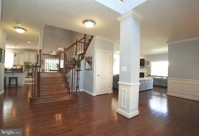 foyer entrance featuring crown molding, dark wood-style flooring, stairway, and ornate columns