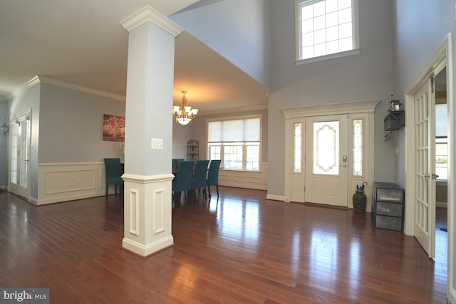 entrance foyer featuring a notable chandelier, dark wood-style flooring, ornamental molding, wainscoting, and ornate columns