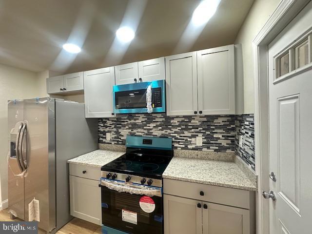 kitchen featuring light stone counters, recessed lighting, white cabinetry, appliances with stainless steel finishes, and tasteful backsplash