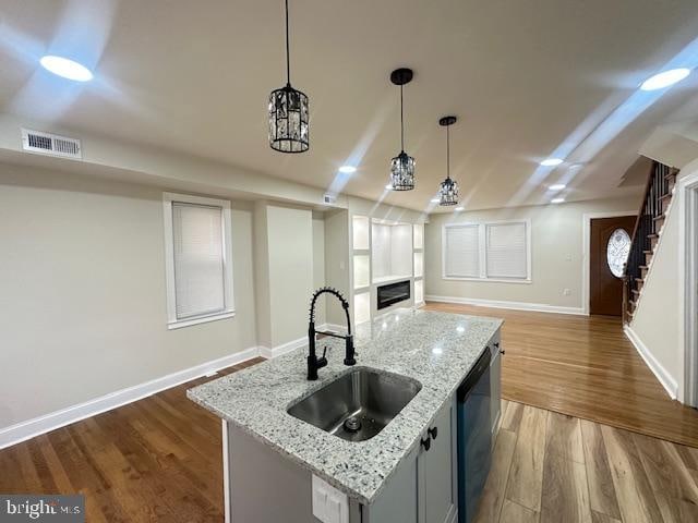 kitchen featuring a center island with sink, wood-type flooring, hanging light fixtures, sink, and light stone counters