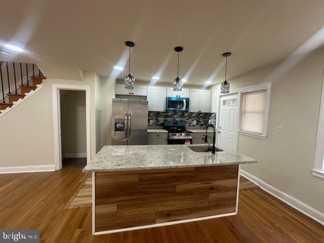 kitchen with stainless steel appliances, white cabinets, a kitchen island, a sink, and light stone countertops