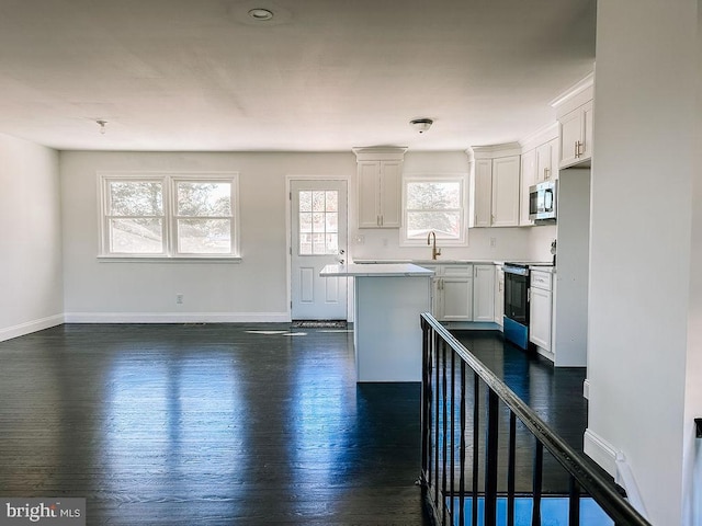 kitchen with range with electric cooktop, a kitchen island, white cabinets, light countertops, and stainless steel microwave