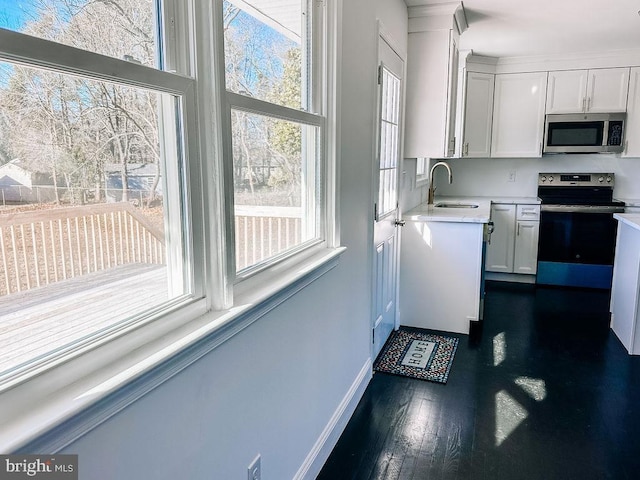 kitchen with dark wood-style floors, appliances with stainless steel finishes, light countertops, white cabinetry, and a sink