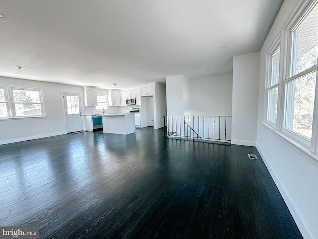 unfurnished living room with dark wood-style floors, visible vents, baseboards, and a sink