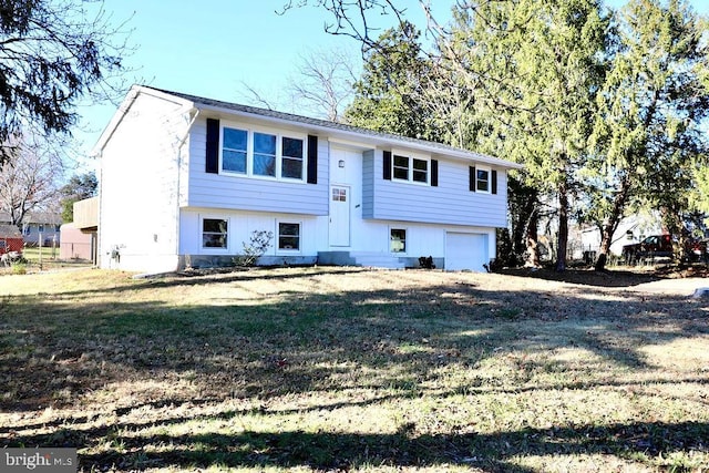 bi-level home with a garage, dirt driveway, and a front lawn