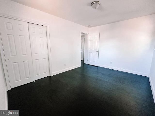 unfurnished bedroom featuring dark wood-style flooring, a closet, and baseboards