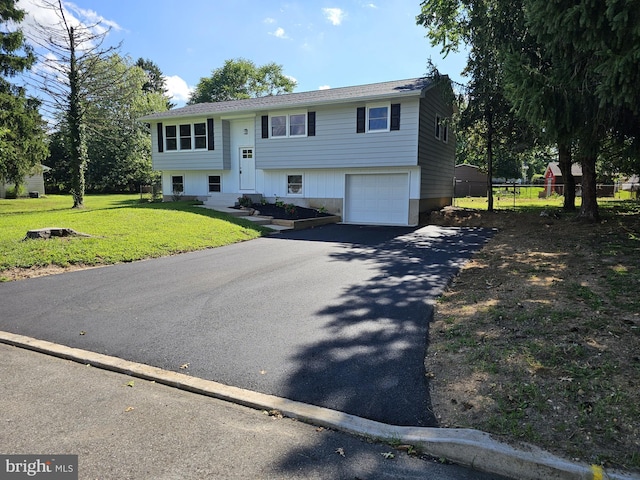 bi-level home featuring a garage, driveway, a front yard, and fence