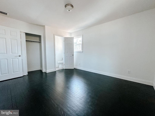 unfurnished bedroom featuring dark wood-style flooring, a closet, visible vents, ensuite bath, and baseboards