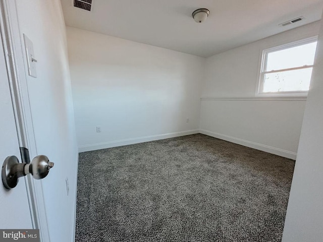 spare room with dark carpet, visible vents, and baseboards