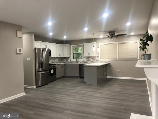 kitchen featuring dark wood-type flooring, ceiling fan, stainless steel appliances, kitchen peninsula, and pendant lighting