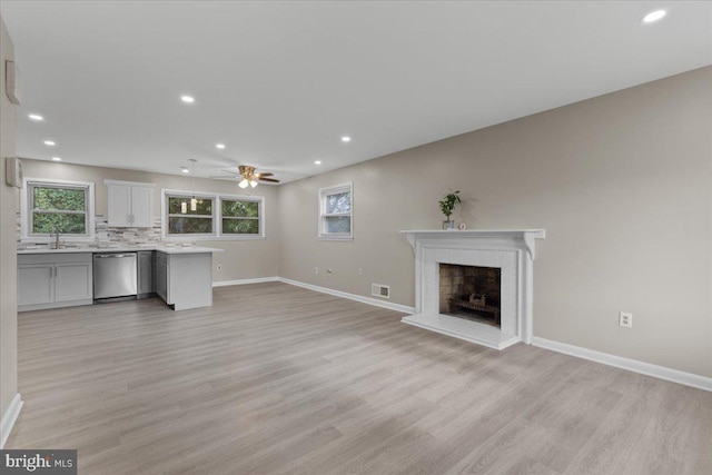 unfurnished living room with light hardwood / wood-style flooring, a healthy amount of sunlight, and a brick fireplace