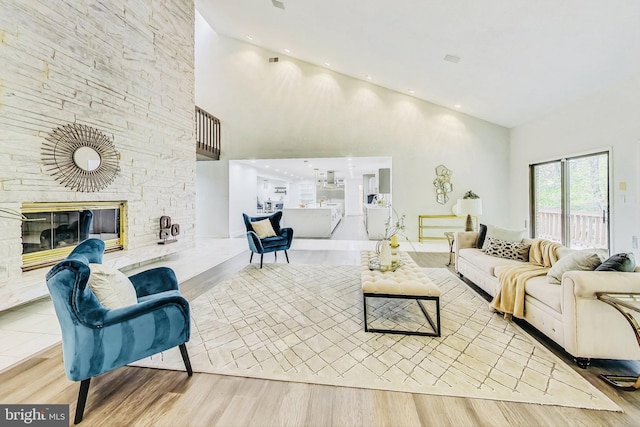 living room with a high ceiling, a stone fireplace, and wood finished floors