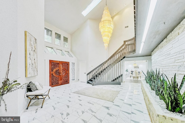 foyer entrance featuring an inviting chandelier, a towering ceiling, and a skylight