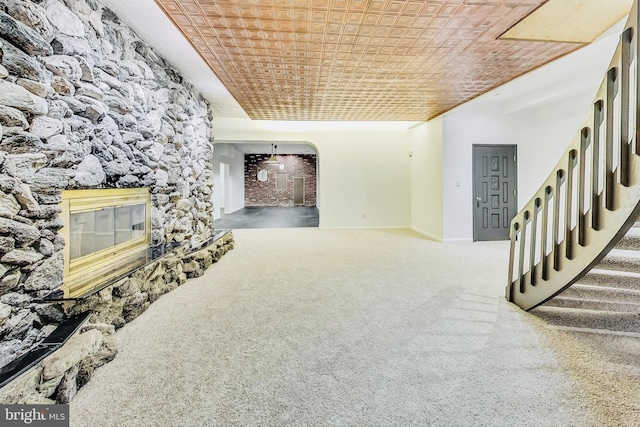 unfurnished living room featuring stairs, a stone fireplace, carpet, and baseboards