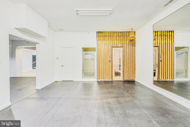 unfurnished room with baseboards, visible vents, arched walkways, and finished concrete floors