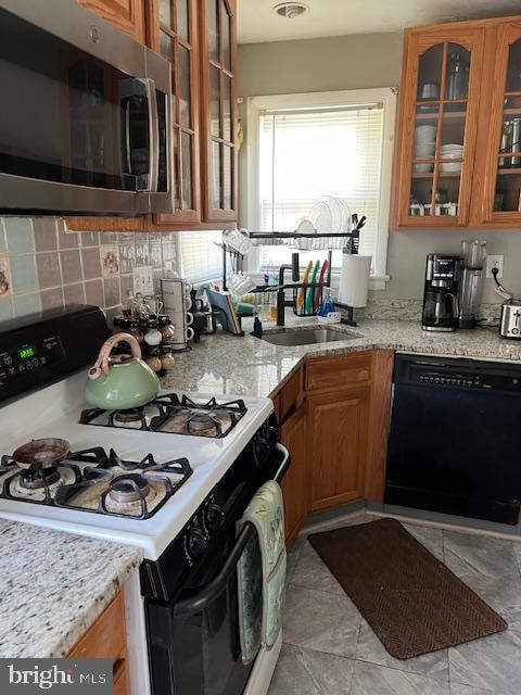 kitchen featuring light stone countertops, black dishwasher, white gas range oven, and sink